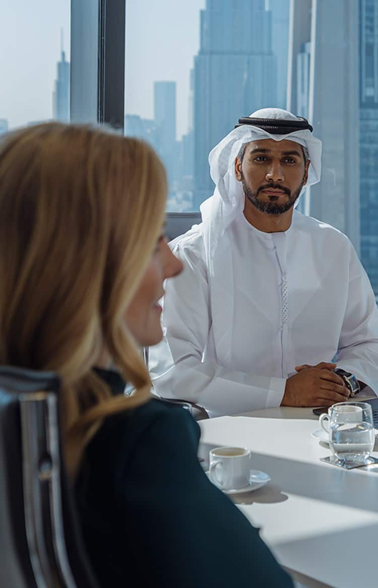 Corporate team collaborating in a meeting with Dubai's skyline visible through the windows