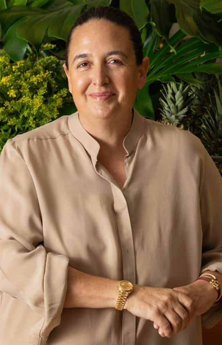Natasha Sideris standing in a stylish workspace with fresh produce and indoor plants behind her