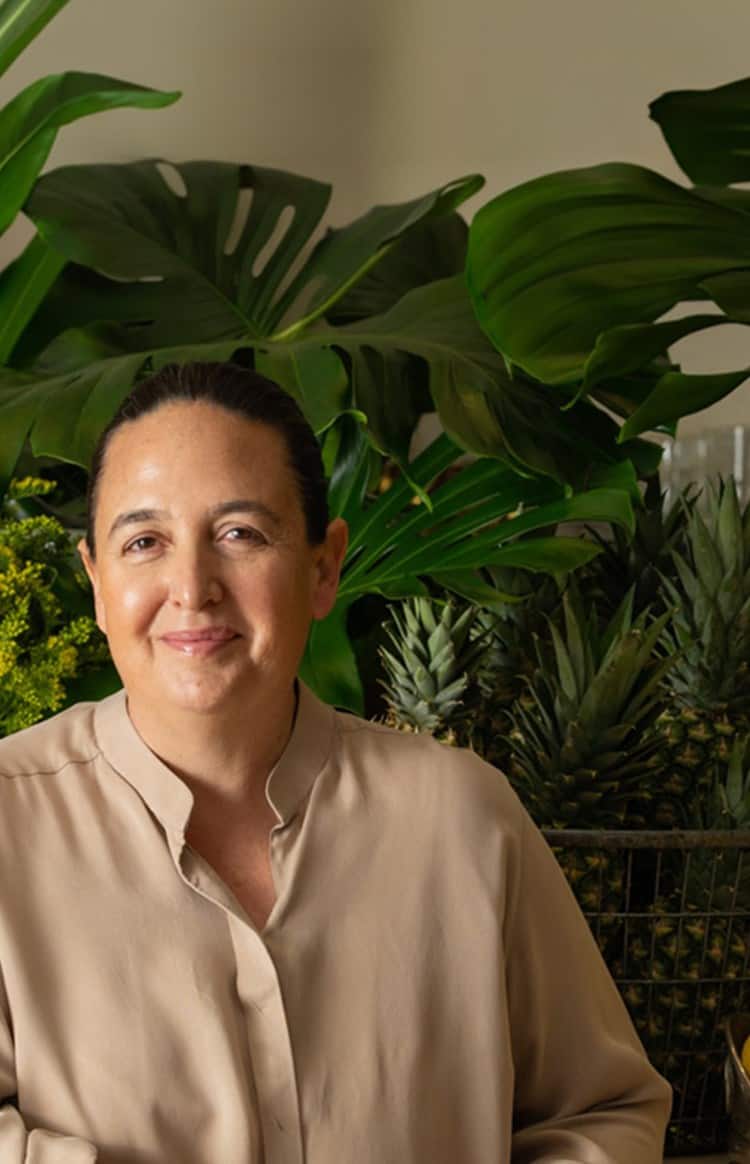 Natasha Sideris standing in a stylish workspace with fresh produce and indoor plants behind her
