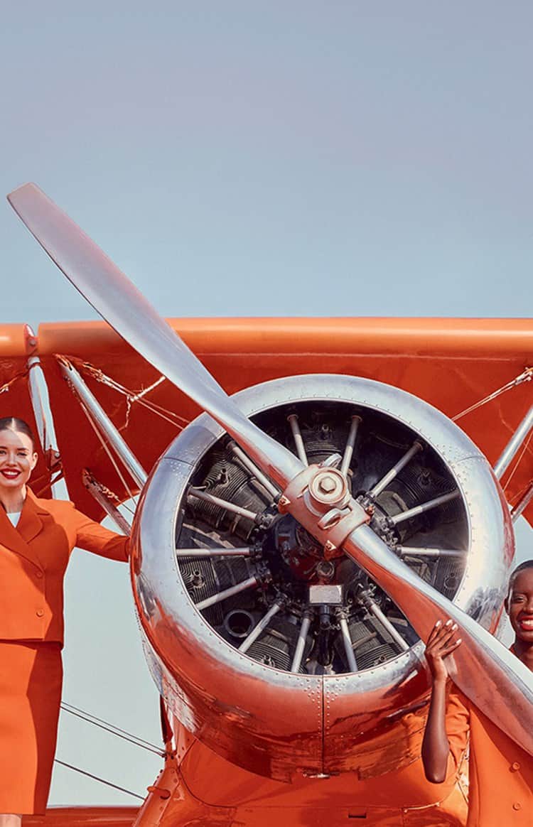 Four women in matching orange uniforms pose around a Jetex propeller aircraft on a runway