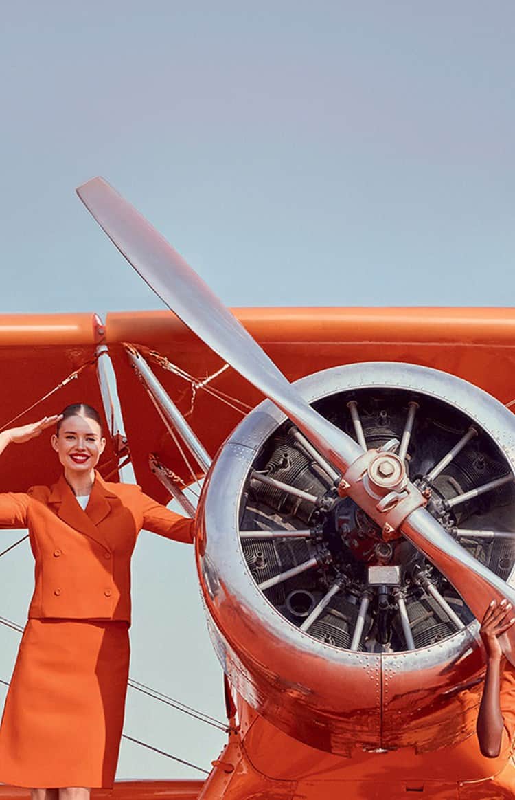 Four women in matching orange uniforms pose around a Jetex propeller aircraft on a runway
