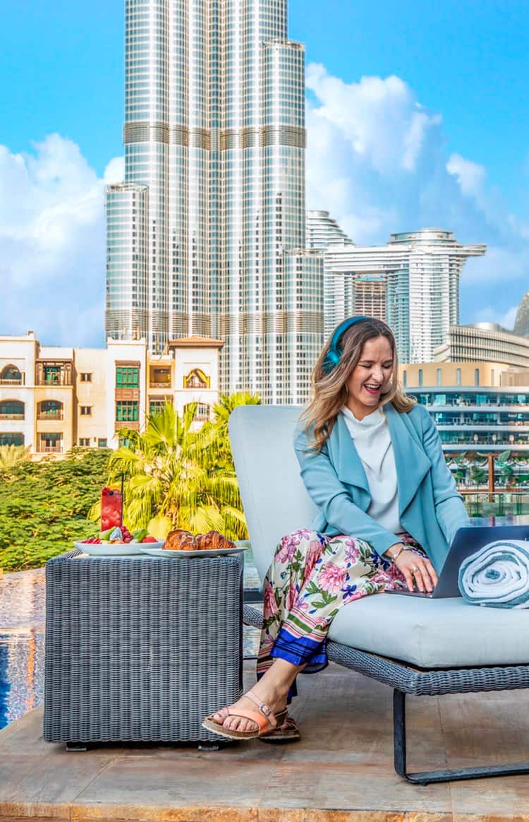 Woman working remotely by a pool overlooking Dubai