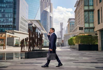 Business professional walking through Dubai's modern financial district with skyscrapers in the background