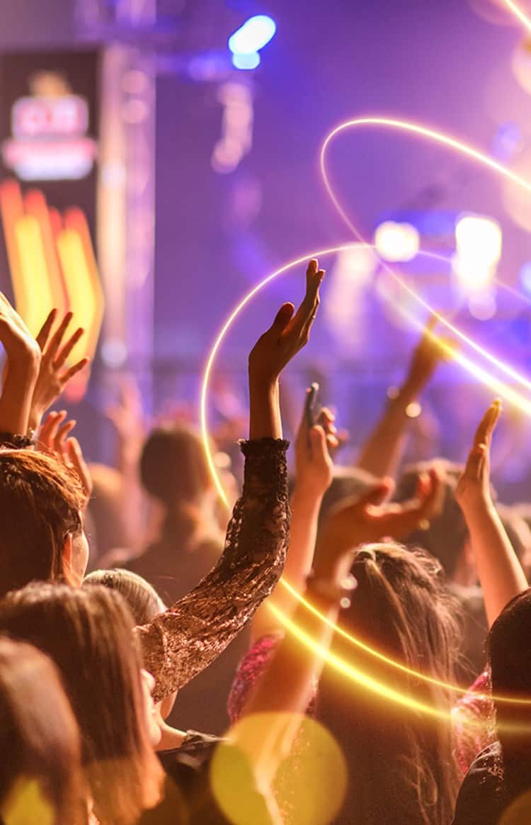 Audience raising their hands during a live concert with colourful stage lighting