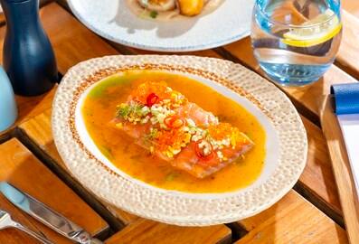 A vibrant citrus crudo fish dish garnished with chili and herbs, served on a textured plate at The Beach House